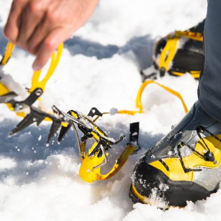 Ein Mann legt an seine steigeisenfesten Wanderschuhe Steigeisen an